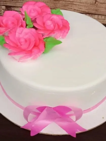 A simple and elegant cheesecake with a glossy white finish. It's topped with delicate pink sugar roses and a ribbon, perfect for any occasion.