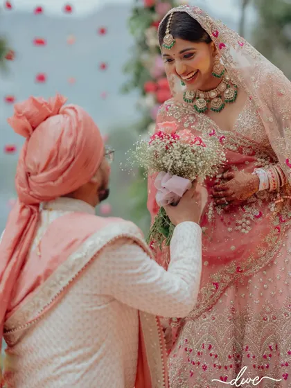 A heartwarming moment as the groom gets down on one knee with a bouquet for his bride during their lakeside wedding ceremony.
