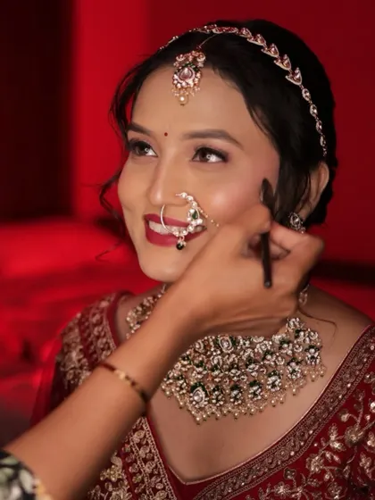 A candid moment during the makeup process, capturing the bride's beautiful smile.