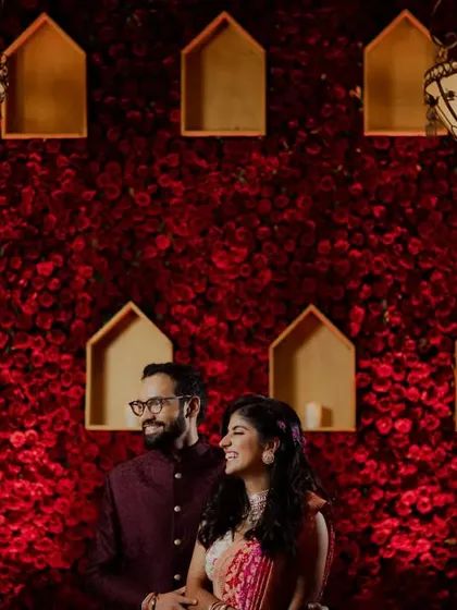 The couple posing against a grand red rose wall that our team designed and executed.