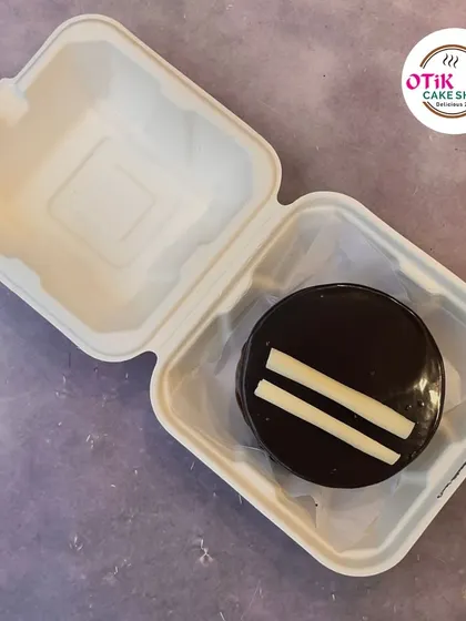 A sleek and simple chocolate bento cake. The glossy ganache finish is accented with two white chocolate strips for a modern, minimalist look.