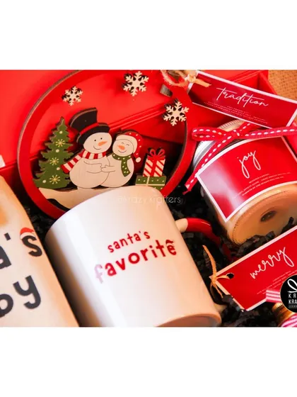 A close-up of the 'Holiday Home' hamper, showing the 'Santa's Favorite' mug and snowman-themed plate.