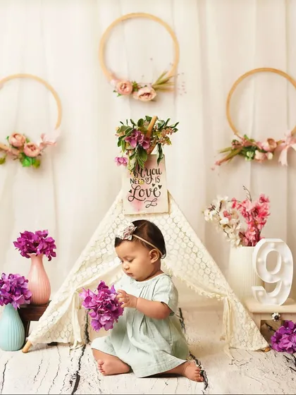 A nine-month milestone session with a lovely boho-floral theme. The baby girl explores the purple flowers in front of a lace teepee.
