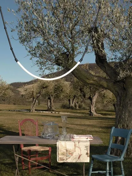 The Leda outdoor light hung between trees, illuminating a rustic picnic table. This flexible system allows you to bring beautiful, high-design lighting to any part of your property.
