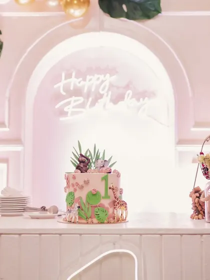The jungle-themed cake displayed on a clean, white dessert bar in front of a "Happy Birthday" neon sign. The elegant setup highlights the custom cake.