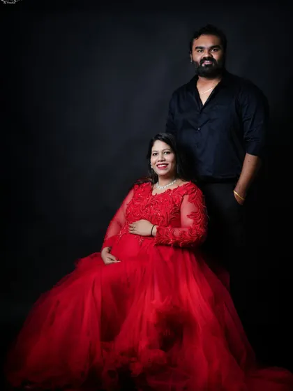A classic seated portrait of the couple. The woman's stunning red gown is the centerpiece, while her partner stands beside her, creating a formal and elegant composition.