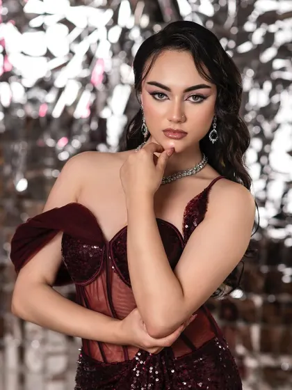 A modern and glamorous beauty portrait. The sharp, winged eyeliner and glossy lips are the stars here, set against a sparkling silver background that adds to the high-fashion feel.