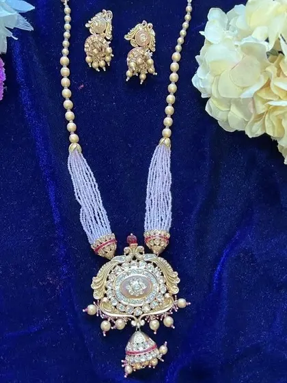 A beautiful long necklace made with a large Kundan pendant and strands of tiny white beads. This piece is perfect for layering or wearing on its own for a graceful, traditional look.