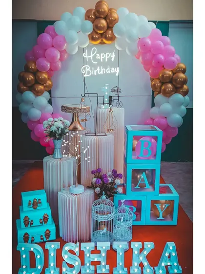 A classic pink, white, and gold first birthday setup. This timeless design includes a balloon ring, 'BABY' blocks, and marquee letters.
