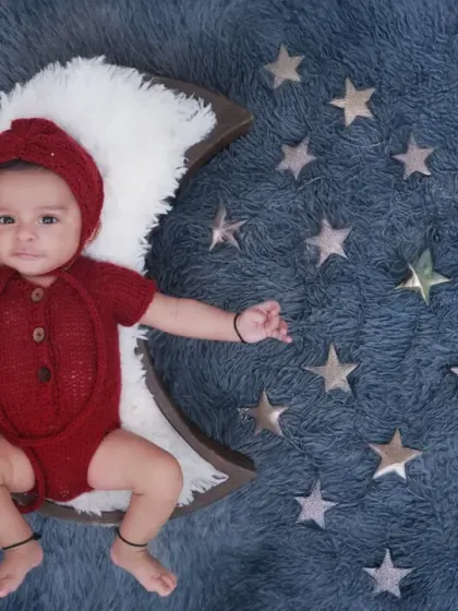 A "Twinkle Twinkle Little Star" themed newborn shoot. Here, the baby is dressed in a cute red outfit, resting on a crescent moon prop against a starry blue background.