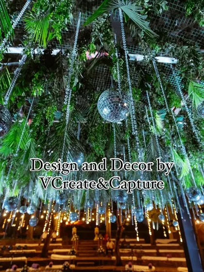 A stunning ceiling treatment for an outdoor sangeet, featuring a dense canopy of green leaves and dozens of hanging disco balls that sparkle in the light.