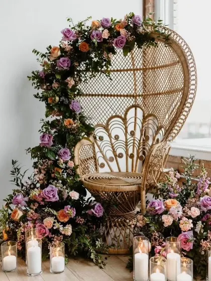 A close-up of the peacock chair, adorned with a lush floral garland and surrounded by candles. This creates a beautiful and regal focal point for a baby shower, perfect for photos.
