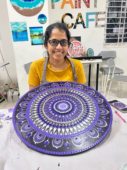 A participant proudly displays her large, intricate purple mandala dot painting, created in the studio.