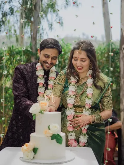 A happy couple cutting their cake at an outdoor engagement, framed by a curtain of hanging flowers.