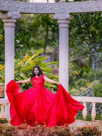 A moment of pure joy and movement. The bride-to-be twirls in her magnificent red gown at the classic white pillar setup, creating a dynamic and happy pre-wedding portrait.