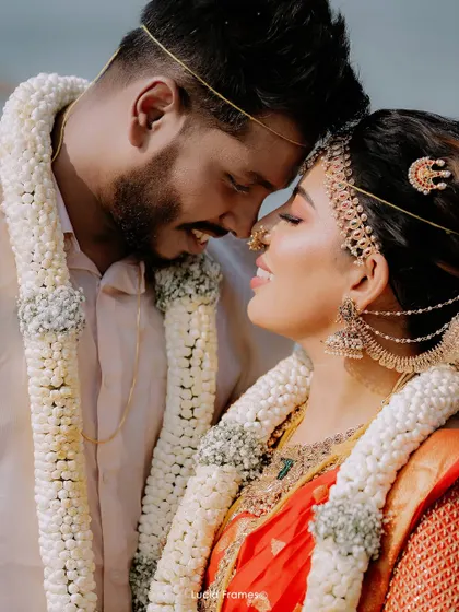 An intimate close-up of the couple, their faces close, adorned with beautiful garlands after their beach ceremony.