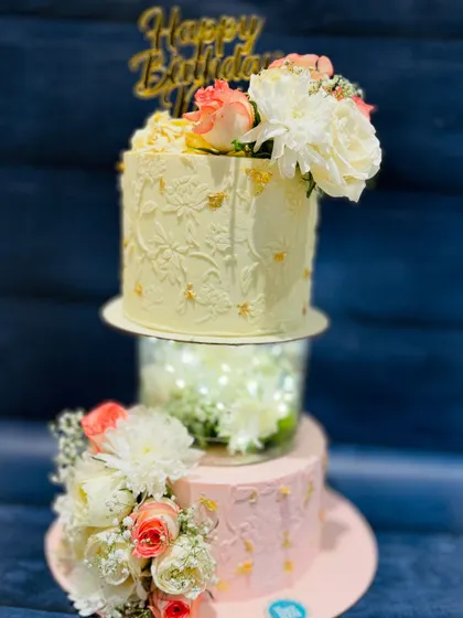 An exquisite two-tier cake for a 50th birthday. The design features a separator tier filled with lights and is adorned with beautiful fresh flowers for a royal and celebratory feel.