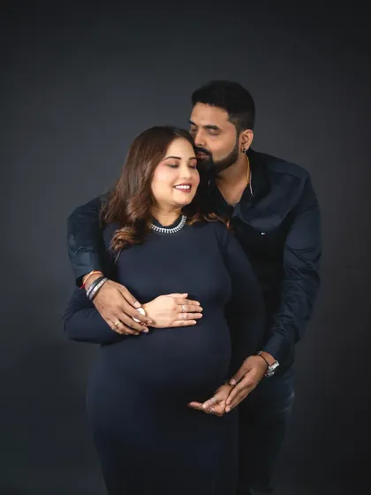 A sweet and gentle moment captured against a classic dark backdrop. The focus is entirely on the couple's loving embrace and the beautiful baby bump.