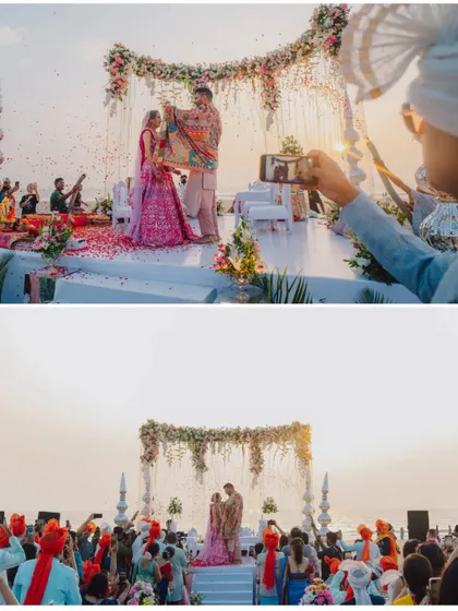 The Varmala ceremony set against the setting sun in Goa. The entire scene, with guests capturing the moment, is filled with the magic of a destination sundowner wedding.
