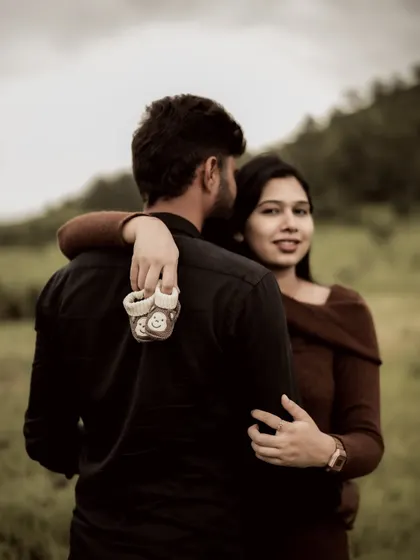 A playful over the shoulder shot. The mom-to-be looks back with a smile while holding a pair of baby shoes, a subtle and sweet pregnancy announcement.