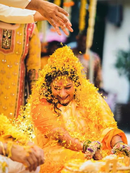 A beautiful shot of the bride being showered with flower petals during her Haldi ceremony. Her happy expression shows the joy of being surrounded by loved ones.