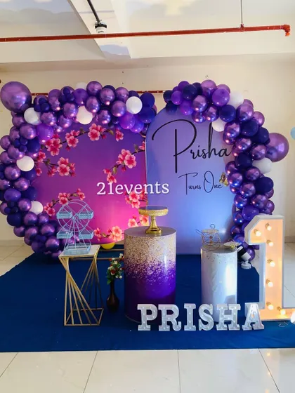 A beautiful purple floral and butterfly theme for a first birthday. The setup includes two backdrops and a glittery pedestal.
