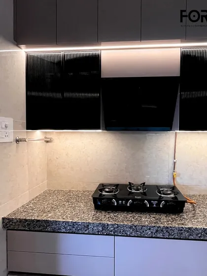 A view of the cooking area with a modern chimney hood set against glossy, fluted cabinet doors. The LED strip lighting provides excellent task lighting over the granite countertop.