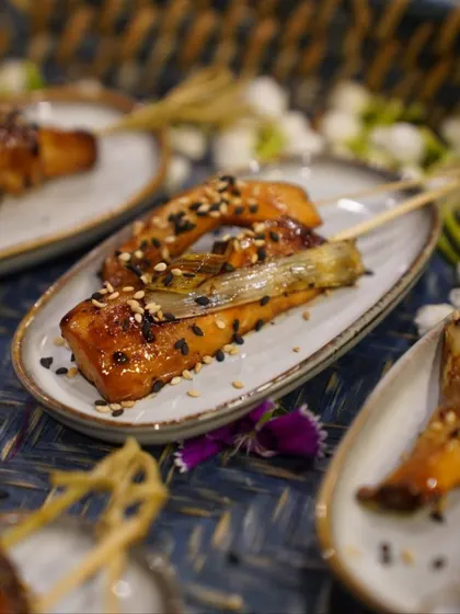 A skewer of glazed salmon, sprinkled with black and white sesame seeds. This appetizer combines sweet and savory flavors with a beautiful presentation, perfect for an elegant cocktail party or corporate event.