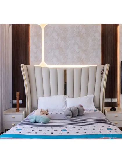This bedroom features a grand, wingback-style upholstered headboard that makes a luxurious statement. The textured wall panels and integrated lighting behind the bed add depth and a warm, ambient glow.