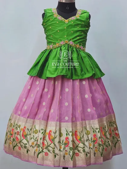 A beautiful pattu pavadai with a Paithani border. The pink organza skirt features a woven border with colorful parrots, paired with a simple green peplum top.