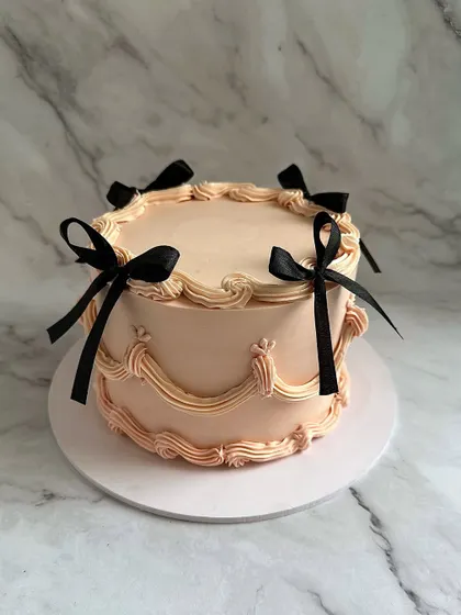 A soft, peach-toned vintage cake with classic swag piping and elegant black satin bows. This design is perfect for a sophisticated and stylish celebration.