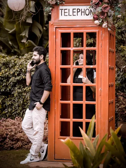 A playful pre-wedding photo featuring a classic red telephone booth, with the couple pretending to be on a call, adding a touch of British vintage charm.