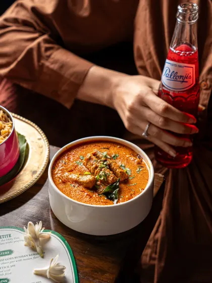 A lifestyle shot featuring Salli Murghi and Pallonji's soda at Gallops. The inclusion of a person adds a relatable touch, helping viewers imagine themselves enjoying the meal.