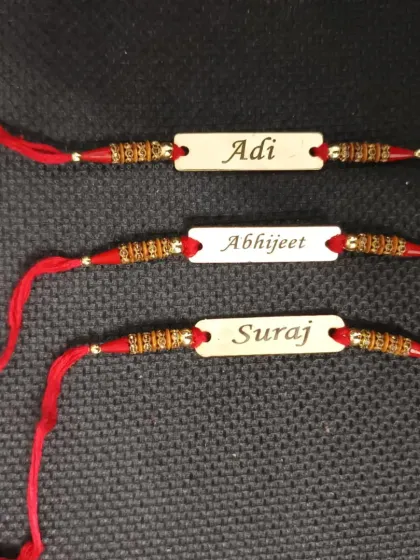 Simple and classic wooden name rakhis on a traditional red thread.