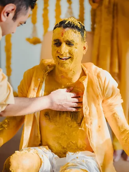 The groom smiles as friends and family apply turmeric paste during his Haldi ceremony.