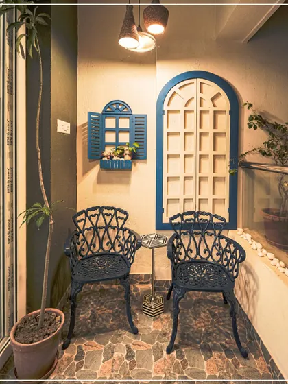 A charming balcony nook with blue and white decorative window frames and cast iron chairs, creating a Mediterranean-inspired feel.