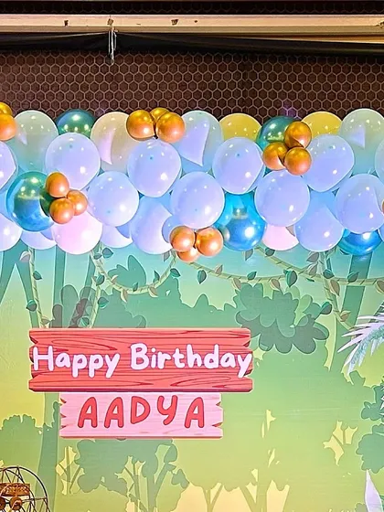 A close-up of a jungle-themed backdrop with a custom 'Happy Birthday' sign. The balloon garland on top adds a pop of color.