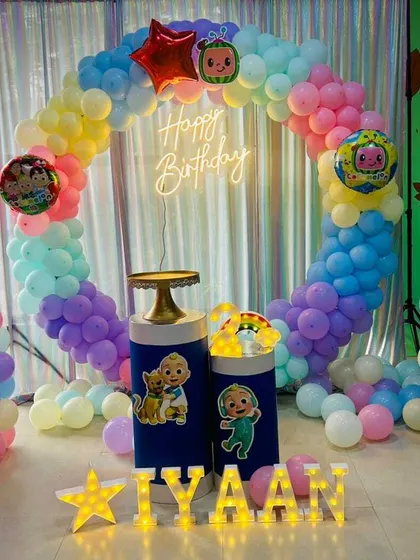 A Cocomelon themed birthday party with a pastel rainbow balloon ring. This setup combines characters from Cocomelon and Masha and the Bear.