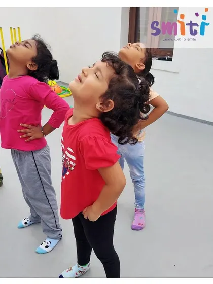Girls practice a gentle warm-up exercise during a structured sports session. These activities help them identify different body parts and improve coordination.