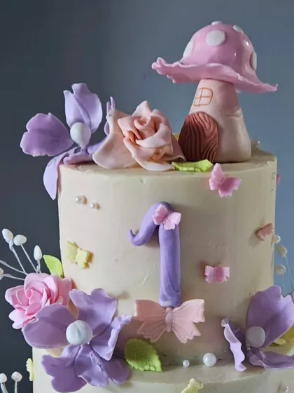 A close-up of the top of the enchanted garden cake, showing the whimsical, edible mushroom house and the arrangement of handcrafted sugar flowers and butterflies.