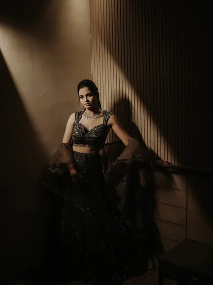 An elegant solo portrait of the bride at her Sangeet. The dramatic lighting sculpts her form, showcasing her stunning gown and poised demeanor in a beautifully artistic way.