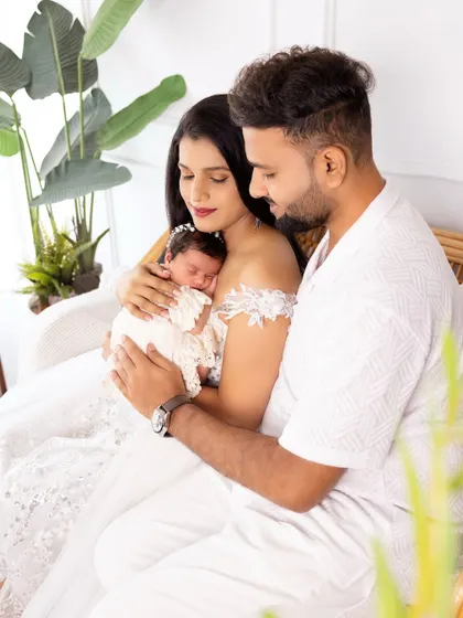 A serene family photo with the parents lovingly gazing at their newborn baby, who is nestled safely in their arms.
