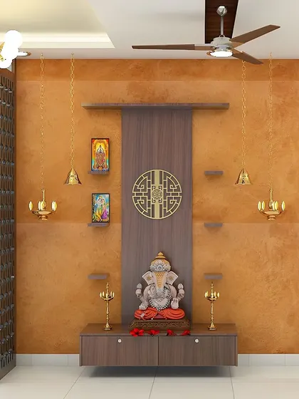 A beautiful pooja unit set against a warm, textured orange wall. The floating console and asymmetrical shelves create a modern yet traditional space for prayer.