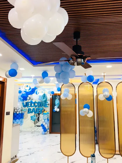 A view from inside the house, looking towards the 'Welcome Baby' backdrop. The ceiling is decorated with floating balloon clusters.