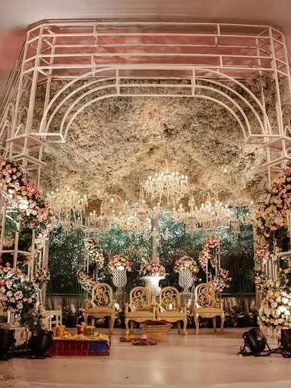 A modern, structural mandap with a canopy of dense, rustic foliage and dozens of hanging crystal chandeliers. The design blends natural textures with glamorous elements for a unique and romantic effect.