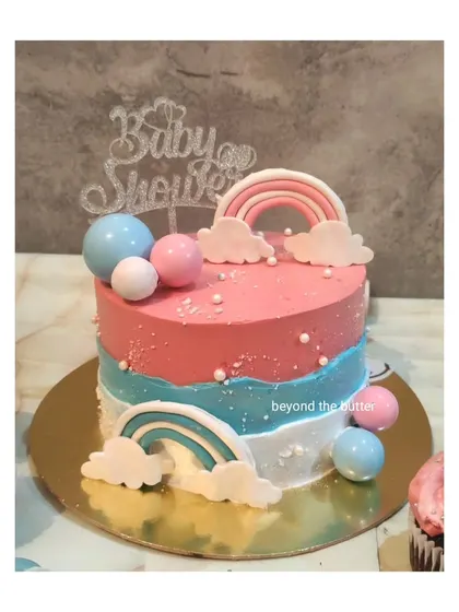 A simple and sweet baby shower cake with a rainbow theme. The pink and blue layers are decorated with fondant rainbows and clouds, perfect for a gender neutral celebration.