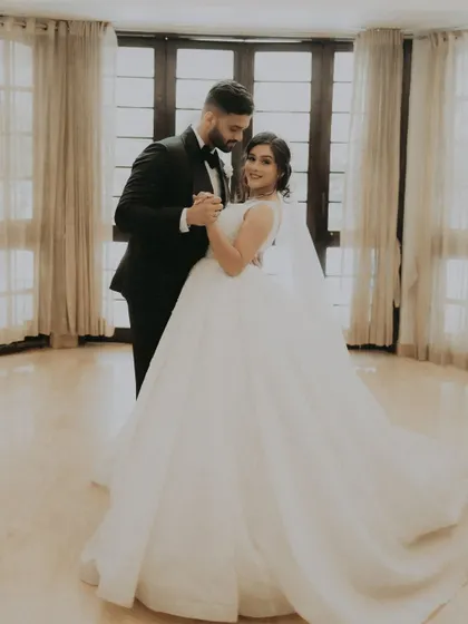 A classic portrait of the couple sharing their first dance in a beautifully lit room, the bride's ball gown in full view.