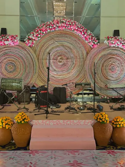 A unique stage backdrop made of large, colorful woven discs and adorned with pink floral arrangements. This adds a modern, artistic touch to an otherwise traditional event.