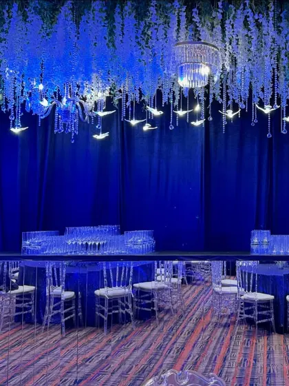 A mirrored bar counter reflects the celestial decor, including cascading white flowers and illuminated bird figures. This setup combines functionality with fantasy, creating a dazzling service area for guests.