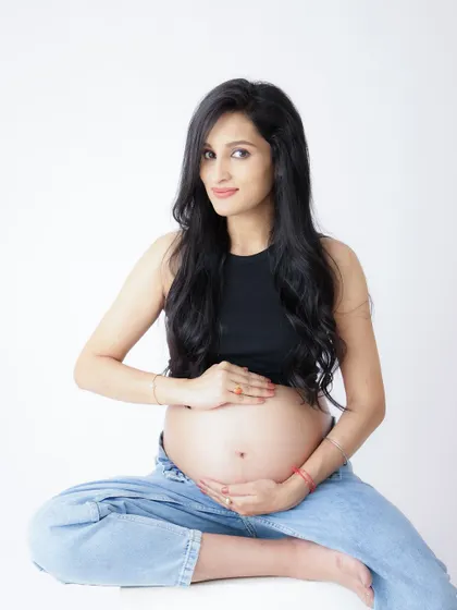 A modern and confident portrait. The mom-to-be smiles at the camera, her casual crop top and jeans look showcasing her bump with style.